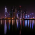 A city skyline at night reflected in the water